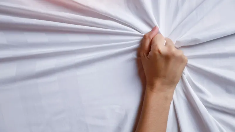 Close up young woman hands pulling white sheets in ecstasy Close up young woman hands pulling white sheets in ecstasy