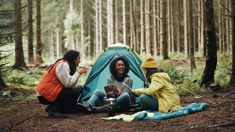 Smiling group of young female friends sitting at their forest campsite 