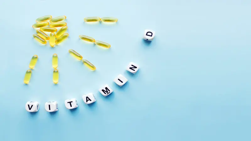 Yellow capsules in the form of the sun with rays and word vitamin D from white cubes with letters on blue background Yellow capsules in the form of the sun with rays and word vitamin D from white cubes with letters on blue background