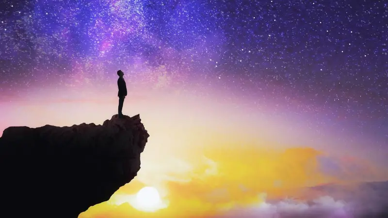 Man standing on edge of cliff with colorful sky Man standing on edge of cliff with colorful sky