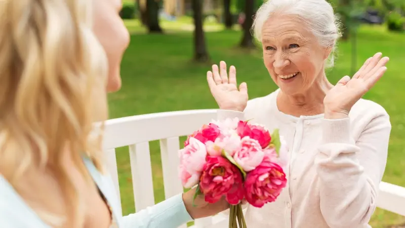 Woman presenting bouquet of flowers to older woman Woman presenting bouquet of flowers to older woman