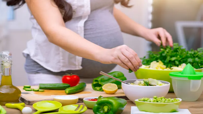 Pregnant person cooking with an assortment of vegetables