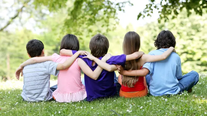 Five children sitting in the grass with arms around each other