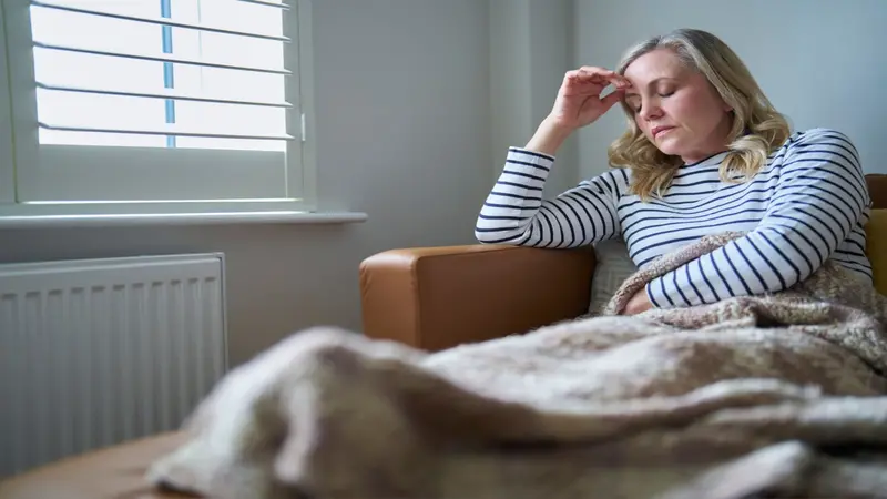 woman sitting on the couch rubbing her head in pain/fatigue, suffering from long COVID woman sitting on the couch rubbing her head in pain/fatigue, suffering from long COVID