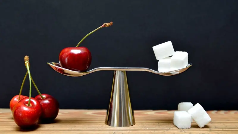 A scale balancing a cherry with sugar cubes