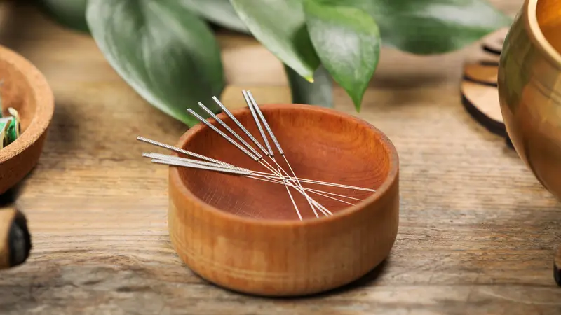 acupuncture needles resting in a wooden bowl