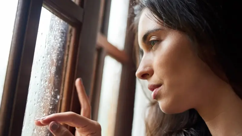 Melancholic woman looks out winter window