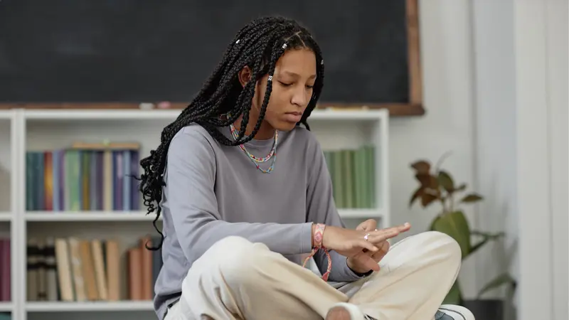 image of Black teenaged girl sitting cross-legged on desk waiting in school library during break