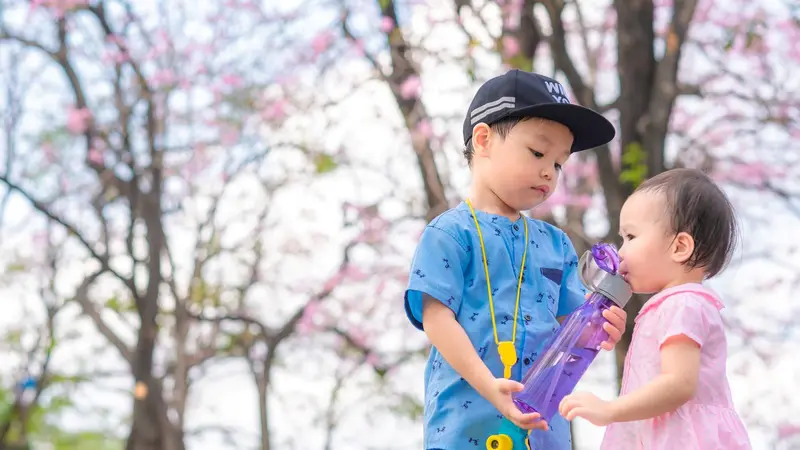 Little boy shares his water with a young girl