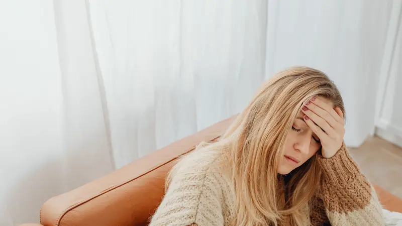 blonde woman sick on couch, holding her head