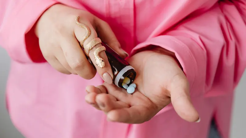 woman in pink shirt emptying medication pills into hands