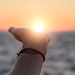 Female hand reaches for the sun at sunset against the background of the sea.
