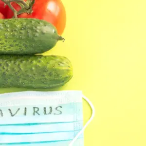 Juicy ripe tomatoes and cucumbers on a green background , next to a protective medical mask with the inscription Coronavirus. 