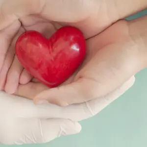 Doctor hands with medical gloves holding child hands and red heart