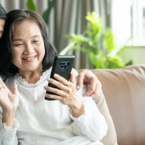 couple sitting on sofa in home playing smartphone and video conference with grandchild