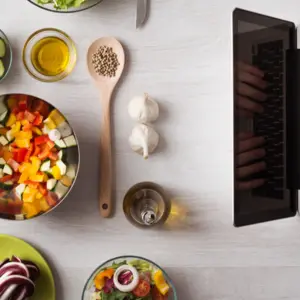 laptop with food ingredients and fresh vegetables on the left, top view