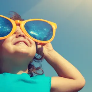 Happy little girl with big sunglasses looking at the sun