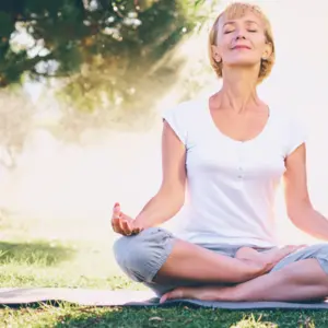 Yoga at park. Senior woman in lotus pose sitting on green grass. 