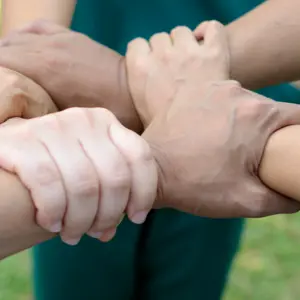 Doctors and nurses in a medical team stacking hands outdoor on the green park background (volunteer)