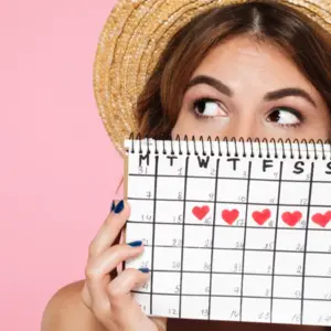 girl in summer hat hiding behind a periods calendar
