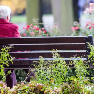 Elderly woman sitting alone on bench in the park