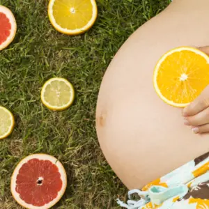 Pregnant woman is laying on grass with fruit