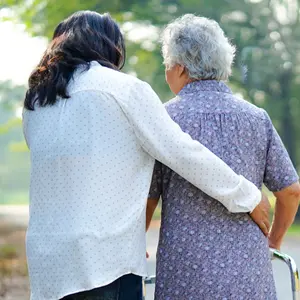 Helping senior woman use walker while walking at park 