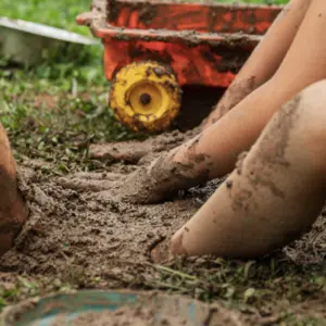 Two boys playing with mud in backyard digging their foot in the dirt.