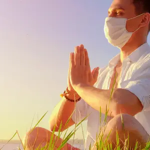 man doing yoga sitting in a lotus pose wearing PPE face mask