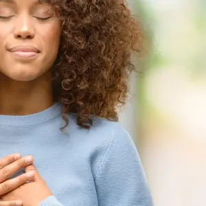 woman wearing a sweater smiling with hands on chest with closed eyes and grateful gesture on face