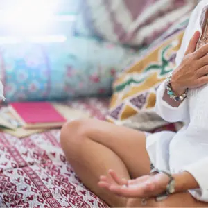 Woman sitting in a lotus position with right hand on heart chakra and left palm open in a receiving gesture