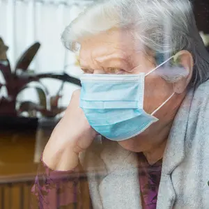 senior woman with surgical mask sitting in window