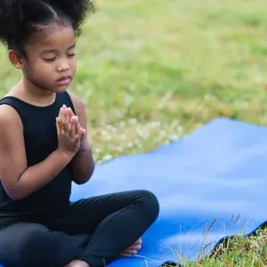 little girl sitting on the roll mat practicing meditate yoga in the park outdoor