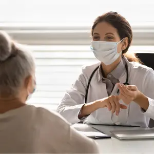 doctor in medical facial mask in consultation with elderly patient during covid-19 pandemic