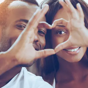 couple sitting close to each other and looking through a heart shape made with their fingers