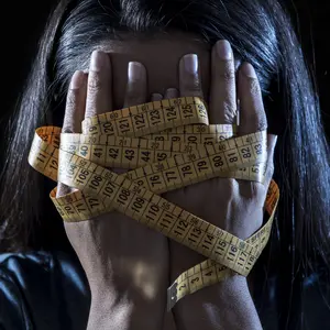 close up hands wrapped in tape measure covering face of young girl suffering nutrition disorder on black background