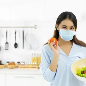Woman Cooking healthy food in the kitchen and wearing COVID face protection mask 
