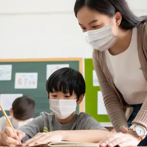 Teacher with little boy wearing protective face masks studying in classroom during COVID-19 pandemic