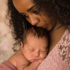 mother in pink lace dress holding her 1 week old little baby