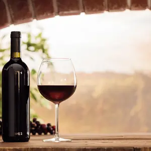 wineglass and bottles next to the window and panoramic view of vineyards at sunset