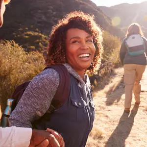 Woman Helping Man On Trail As Group Of Senior Friends Go Hiking In Countryside Together