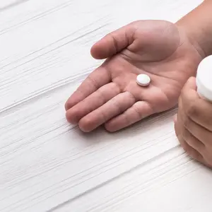 Child hand with white medical pills on wood background
