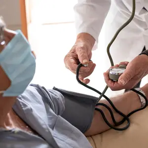 doctor in a white coat takes pressure to an elderly patient with a mask