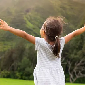 Little girl standing outside, arms raised in gratitude