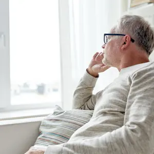 lonely man in glasses thinking and looking through window at home