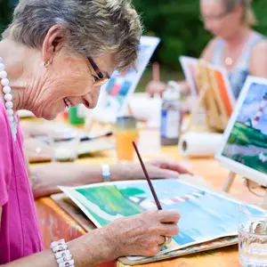 Side view of a happy senior woman smiling while drawing as a recreational activity or therapy outdoors together with the group