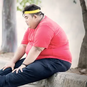 Obese man looks tired after exercising in the park while sitting on the road at autumn time