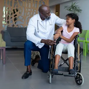 doctor kneeling to talk with girl in wheelchair in hospital foyer. medicine, health and healthcare services.