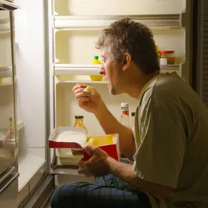 A man with sleep-related eating disorder sleep sits in front of a refrigerator eating out of carton