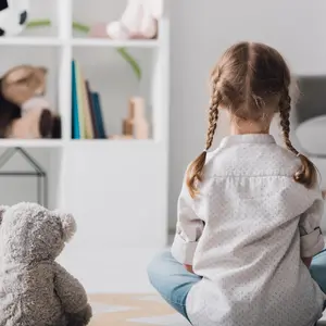Rear view of little child in white shirt sitting on floor with teddy bear practicing mindfulness